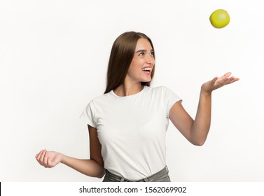 Happy Girl Throwing Apple In The Air Standing Over White Studio Background. Isolated
