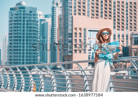 Happy girl traveler looks at the map while walking along the waterfront of the Marina port in Dubai, UAE