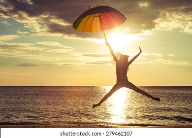 Happy girl with an umbrella jumping on the beach at the sunset time - Powered by Shutterstock