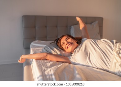 Happy Girl Waking Up In The Morning Sunshine Looking At Sunrise Sun In Window Excited To Enjoy The Day. Wake Up Energetic Asian Woman Lying In Bed Well Rested From A Good Night Sleep.