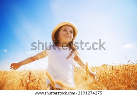 Happy girl walking enjoying the life in the golden field. Nature beauty, sunny blue sky and yelow field of wheat. Family outdoor lifestyle. Freedom concept. Cute little girl in summer field