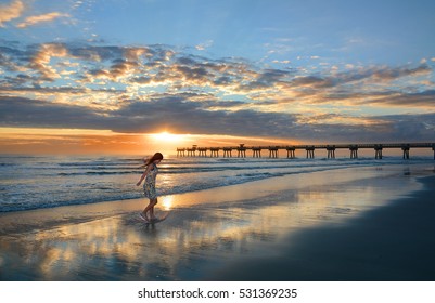 Happy girl walking on the beautiful beach at sunrise,  sun and clouds  reflected on beach. Pier in the background. Jacksonville, Florida, USA.  - Powered by Shutterstock