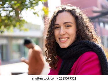 Happy Girl With Wavy Hair Laughing Outdoor With Urban City Context As Background - Millennial Or Gen Z Woman Having Fun Outdoor During Winter Season - Black Man On Background - Focus On Eyes