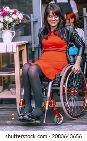 A happy girl in a wheelchair leaves the caf . Optimistic woman with special needs turns the wheels of a wheelchair