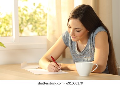 Happy girl writing a letter on a table at home