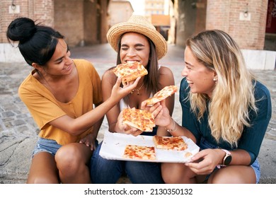 Happy girlfriends eating pizza street food at the city. Female tourist group of three woman having fun. One girl feeds the other. Lifestyle and friendship concept