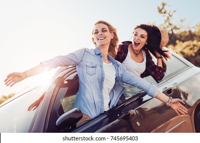 Happy Girlfriends Enjoying On A Long Drive In A Car, Woman With Her Arms Raised.