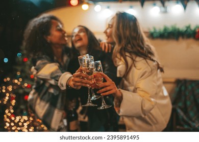 Happy girls celebrating Christmas and New Year winter holidays season outdoor. Young diverse women joyful female friends spending time together have fun drinking sparkling wine near old xmas trailer - Powered by Shutterstock