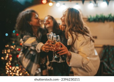 Happy girls celebrating Christmas and New Year winter holidays season outdoor. Young diverse women joyful female friends spending time together have fun drinking sparkling wine near old xmas trailer - Powered by Shutterstock