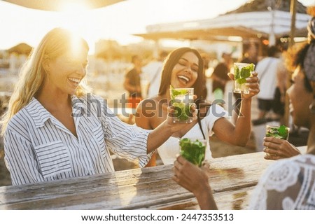 Happy girls cheering with mojitos on the beach at chiringuito sunset party - Summer vacation and people lifestyle concept - Main focus on left female face