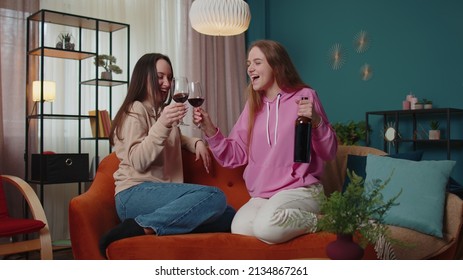 Happy Girls Friends Siblings Clinking Glasses Of Red Wine Cheering And Drinking, Celebrate Birthday Party Hangout At Home In Living Room. Two Female Women Couple Family Celebrating New House Purchase