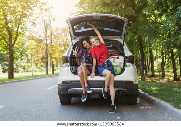 Happy girls sitting in
open car back with salutation gesture. Traveling with friends
concept, copy space