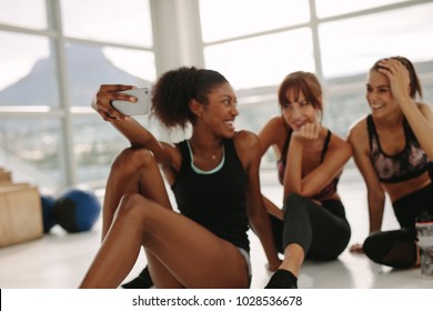 Happy Girls Taking Selfie In Gym. Three Female Friends In Healthclub Taking Selfie With Mobile Phone.