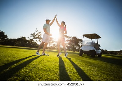 Happy golf player couple giving high five while standing on field