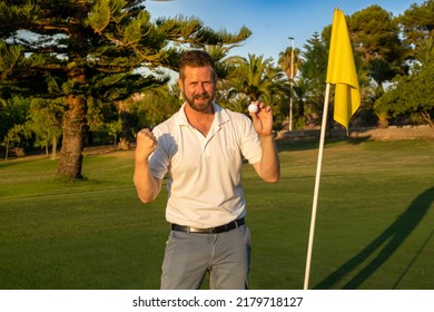 Happy Golf Player Holding The Ball Making Success Gesture At Golf Club.