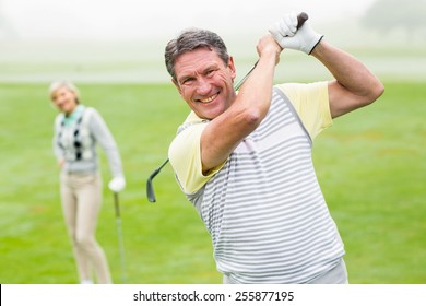 Happy golfer teeing off with partner behind him on a foggy day at the golf course - Powered by Shutterstock