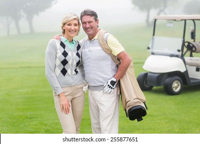 Happy Golfing Couple With Golf Buggy Behind On A Foggy Day At The Golf Course