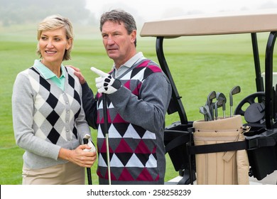 Happy Golfing Couple With Golf Buggy Behind On A Foggy Day At The Golf Course