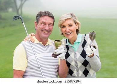 Happy Golfing Couple With Trophy On A Foggy Day At The Golf Course