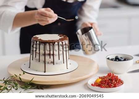 Happy good looking female pastry chef standing with her cake while making. Putting cream on a birthday cake. High quality photo