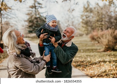 Gutes und aussehendes Ehemann und Ehefrau, die mit ihrem verehrten Enkel im öffentlichen Stadtpark spazieren und spielen