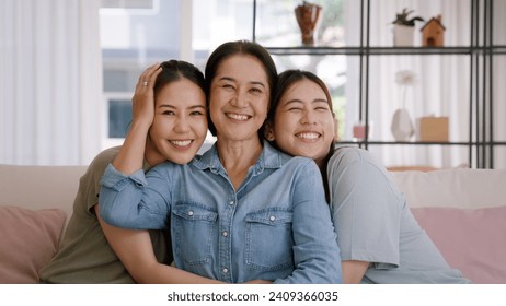 Happy good warm time Mother day two grown up kid child looking at camera cuddle hug arm around mature mum. Love kiss care mom asia middle age adult three people smile enjoy sitting easy at home sofa - Powered by Shutterstock