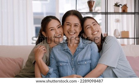 Happy good warm time Mother day two grown up kid child looking at camera cuddle hug arm around mature mum. Love kiss care mom asia middle age adult three people smile enjoy sitting easy at home sofa