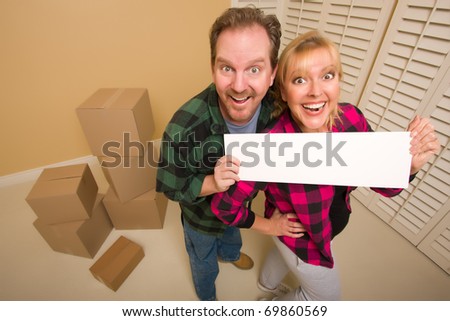 Happy Goofy Couple Holding Blank Sign in Room with Packed Boxes.