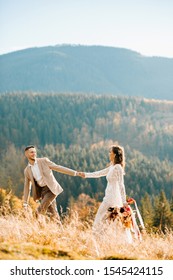 Happy Gorgeous Bride And Groom Walking In Sun Light Holding Hands, Boho Wedding Couple