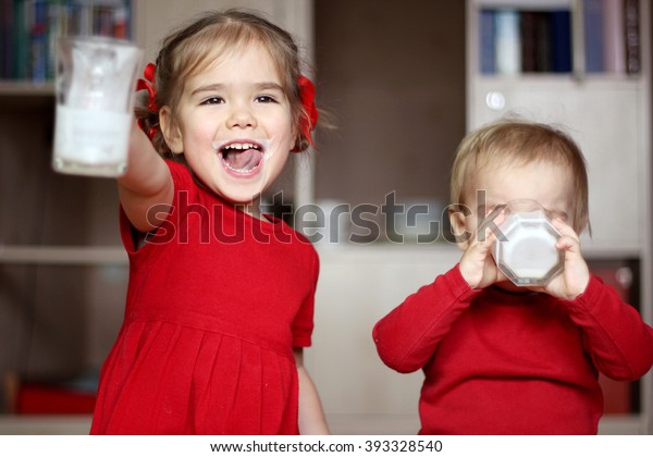 Happy\
gorgeous little girl with milk mustache showing an empty glass\
while her little cute brother drinking a glass of milk at home,\
food and drink concept, healthy food,\
indoor