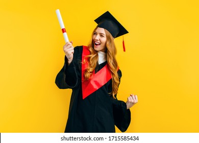 Happy graduate girl with a diploma, shows a gesture of victory and success, on a yellow background.