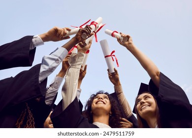 Happy graduate students standing in a circle in black robes and raising their diplomas up to the sky outdoor at graduation ceremony. Education and graduating from university or college concept. - Powered by Shutterstock