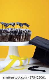 Happy Graduation Day Party Chocolate Cupcakes With Graduation Cap Hat Topper Decorations, In Yellow, Black And White Party Theme. 