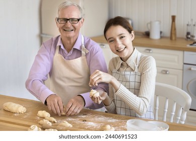 Happy grandad and granddaughter prepare pastries from homemade dough in kitchen, enjoy conversation and cooking process, smile, looking at camera. Portrait of multi generational family cooking at home - Powered by Shutterstock