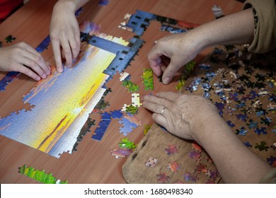 Happy grandchild solving puzzle at home while mature granny, playing together, their hands close-up. Pieces of a puzzle top view. Assembling jigsaw. Children and elderly hands play a board game. - Powered by Shutterstock