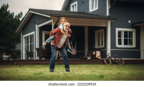 Happy Granddad Enjoying Time Outdoors with His Grandchild, Playing with Energetic Young Girl. Joyful Grandpa Giving a Piggyback Ride on a Lawn in Front of the House.