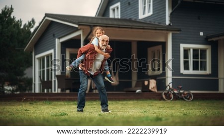 Happy Granddad Enjoying Time Outdoors with His Grandchild, Playing with Energetic Young Girl. Joyful Grandpa Giving a Piggyback Ride on a Lawn in Front of the House.