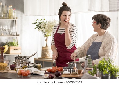 Happy Granddaughter Looking At Her Grandma While Cooking