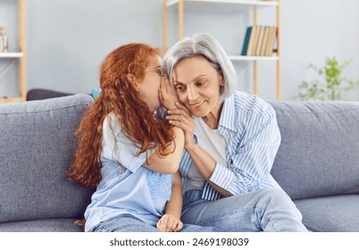 Happy granddaughter whispers a secret or gossip into grandmother ear. This intimate family moment captures the joy of sharing hearsay and talking together, highlighting close bond. - Powered by Shutterstock