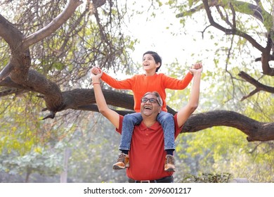 Happy grandfather carrying grandson on shoulders at park
				