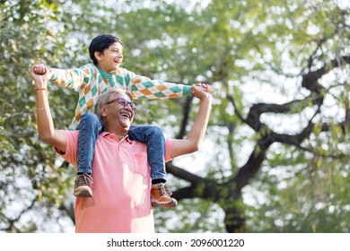 Happy Grandfather Carrying Grandson On Shoulders At Park
