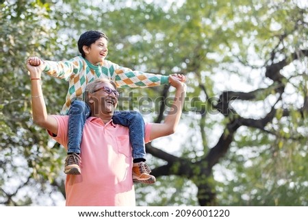 Happy grandfather carrying grandson on shoulders at park

