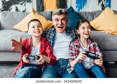 Happy Grandfather...son  And Daughter Playing Video Game While Lying On Floor At Home.