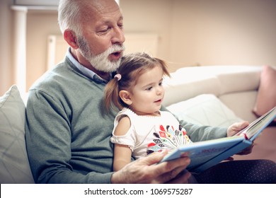 Happy grandfather and granddaughter reading book together at home. Close up.