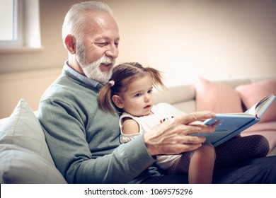 Happy grandfather and granddaughter reading book together at home. Close up. - Powered by Shutterstock