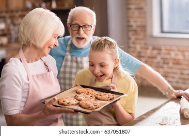 Happy grandfather, grandmother and grandchild looking at tray with delicious cookies - Powered by Shutterstock