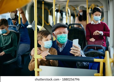 Happy Grandfather And Grandson Wearing Protective Face Masks And Taking Selfie While Commuting By Bus. 