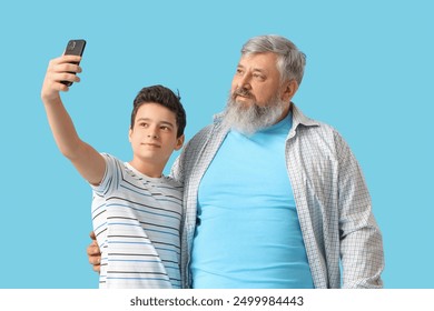 Happy grandfather with his cute grandson taking selfie on blue background - Powered by Shutterstock