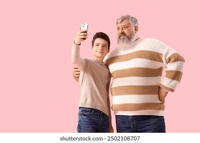 Happy grandfather and his cute grandson taking selfie on pink background - Powered by Shutterstock