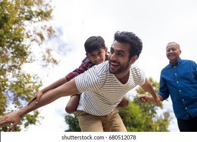 Happy grandfather looking at man giving piggy backing to son with arms oustretched in yard - Powered by Shutterstock